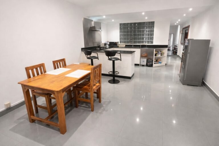 Open-plan kitchen and dining area with wooden dining table, breakfast bar seating, modern countertops, and glossy tiled floors