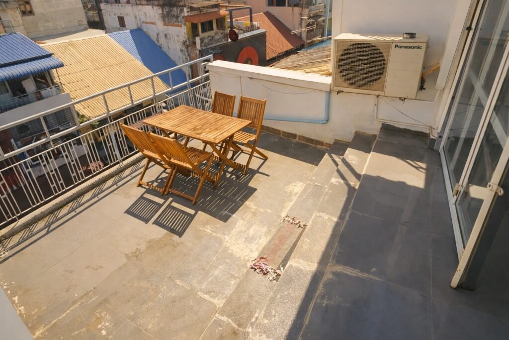 Large private balcony of a Phnom Penh loft apartment with wooden outdoor table and chairs in bright sunlight