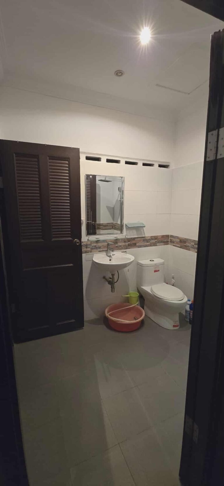 Bathroom with toilet, wall-mounted sink, mirror cabinet, and tiled walls Caption Description