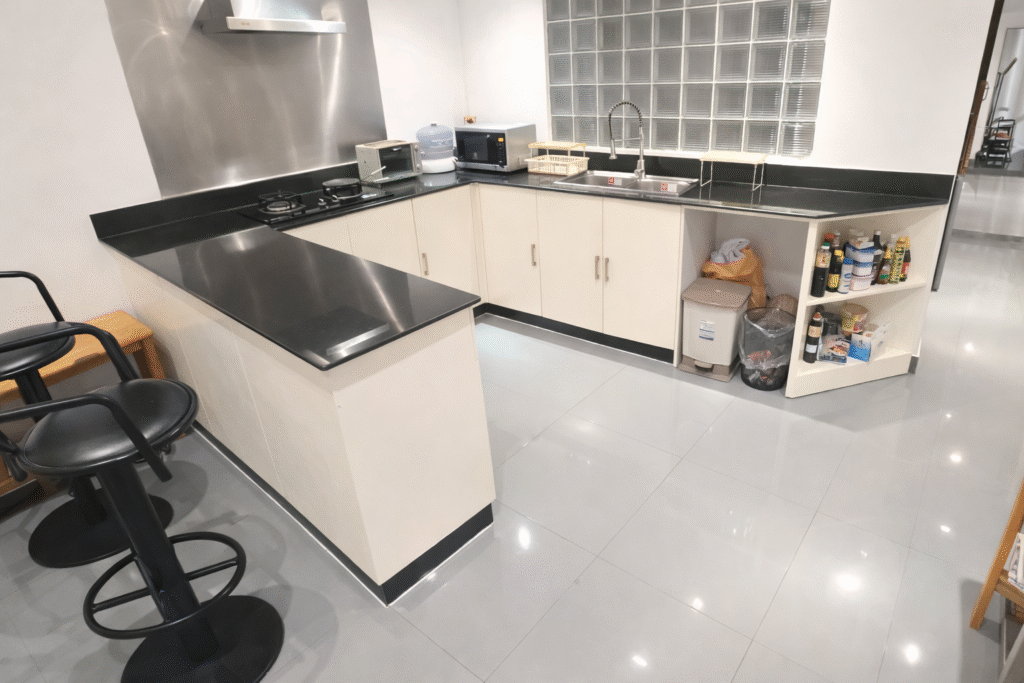 Bright modern L-shaped kitchen with black countertops, white cabinets, glass block window, and reflective gray tile floor. Caption: Description: