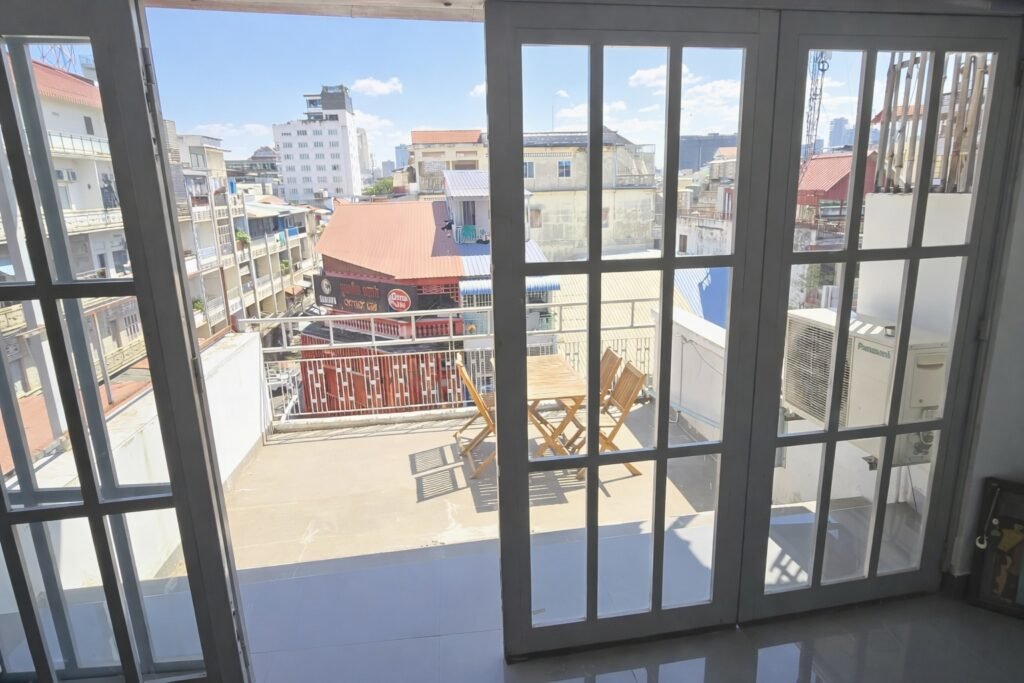 View from inside the living room of a Phnom Penh loft apartment looking out through glass doors to a large private balcony and city skyline