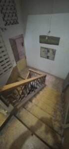 Older apartment building staircase and landing with tiled steps and metal railing on an upper floor