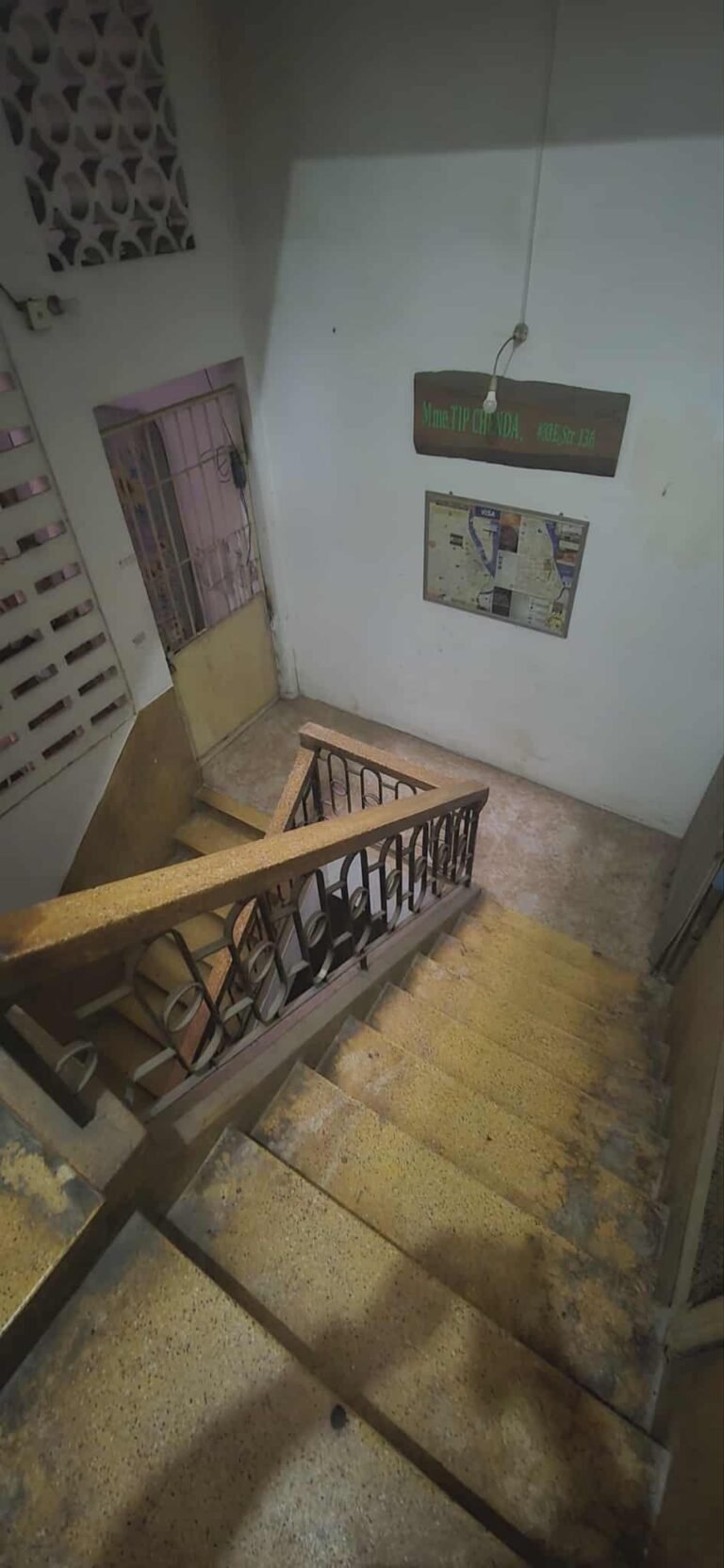 Older apartment building staircase and landing with tiled steps and metal railing on an upper floor