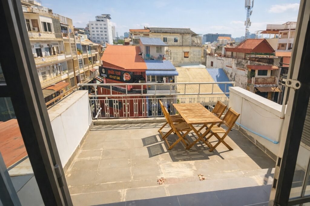 Large private balcony of a Phnom Penh loft apartment with wooden outdoor table and chairs in bright sunlight