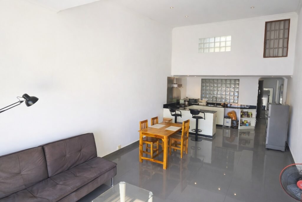 Large private balcony of a Phnom Penh loft apartment with wooden outdoor table and chairs in bright sunlight